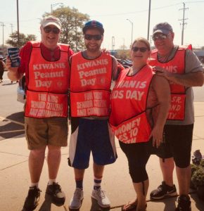 Four people wearing red Kiwanis fundraising vests and standing on a corner